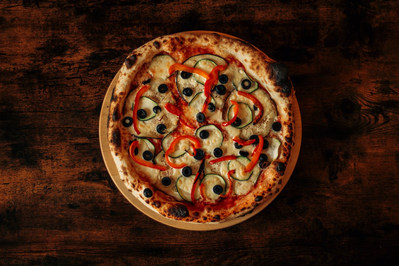 Delicious wood-fired pizza with colorful vegetables, served on a rustic wooden table.